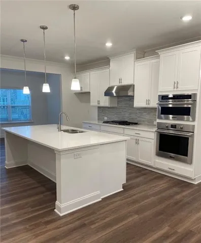 a large kitchen with granite countertop a stove a sink a center island and wooden floor