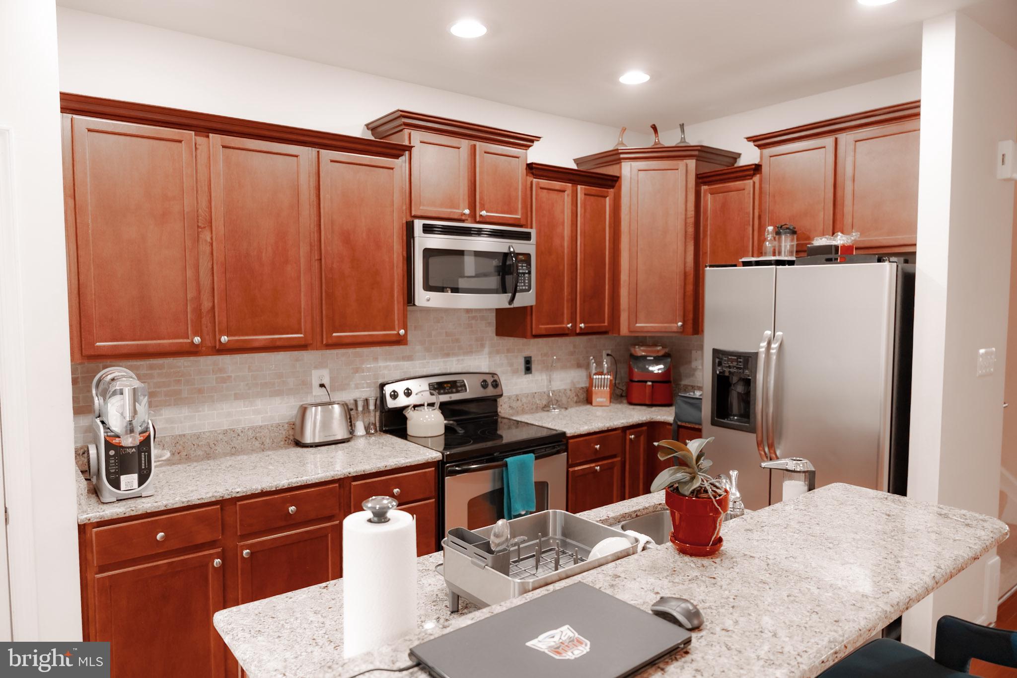 8453 Winding Trail Laurel, MD 20724 - Photo 9 of 24 a kitchen with stainless steel appliances granite countertop a refrigerator a sink a stove a dining table and chairs with wooden floor