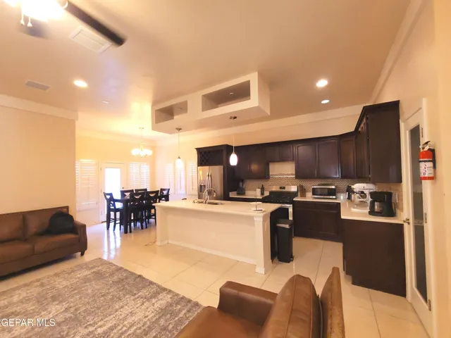 a living room with stainless steel appliances furniture a rug and a kitchen view