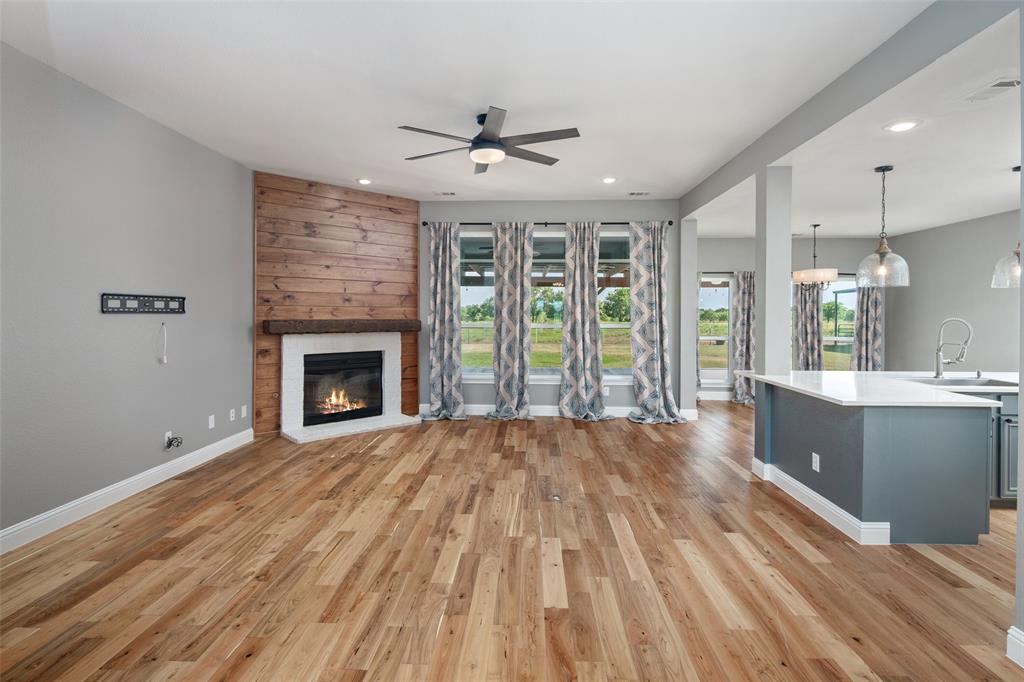 1019 Vaughan Lane Tioga, TX 76271 - Photo 14 of 40 Spacious living area featuring wood-finish flooring, a corner fireplace with a rustic wood-plank accent wall and white mantel, and a ceiling fan