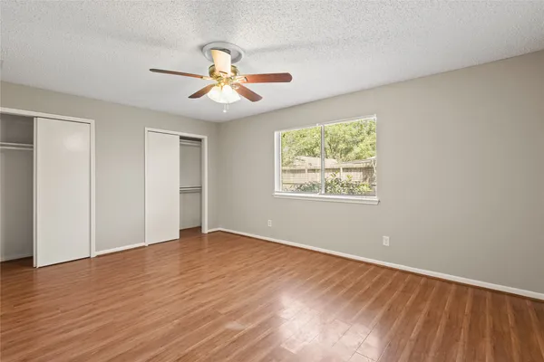 an empty room with wooden floor chandelier fan and windows