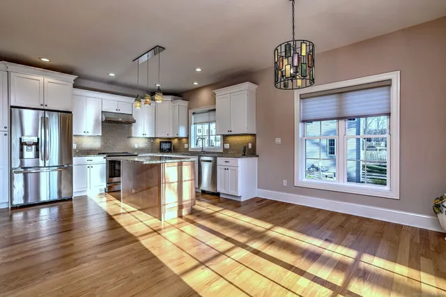 a kitchen with stainless steel appliances granite countertop a refrigerator a sink dishwasher a stove and white cabinets with wooden floor