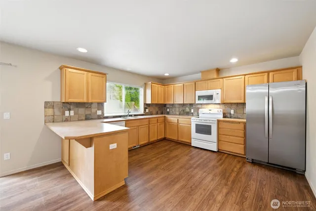 a large kitchen with stainless steel appliances granite countertop a stove a sink dishwasher a refrigerator and white cabinets with wooden floor