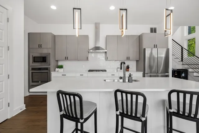 a kitchen with stainless steel appliances granite countertop a table chairs wooden floors and a view of living room