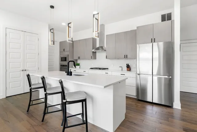 a kitchen with stainless steel appliances a refrigerator a sink and white cabinets with wooden floor