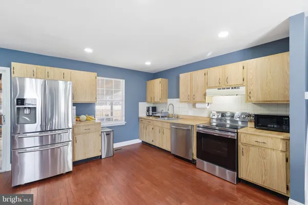 a kitchen with stainless steel appliances granite countertop a stove a sink dishwasher a refrigerator and white cabinets with wooden floor