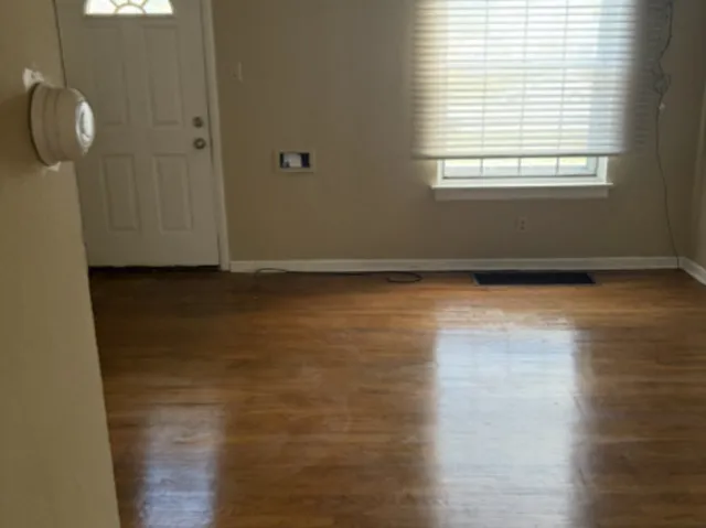a view of an empty room with wooden floor and a window