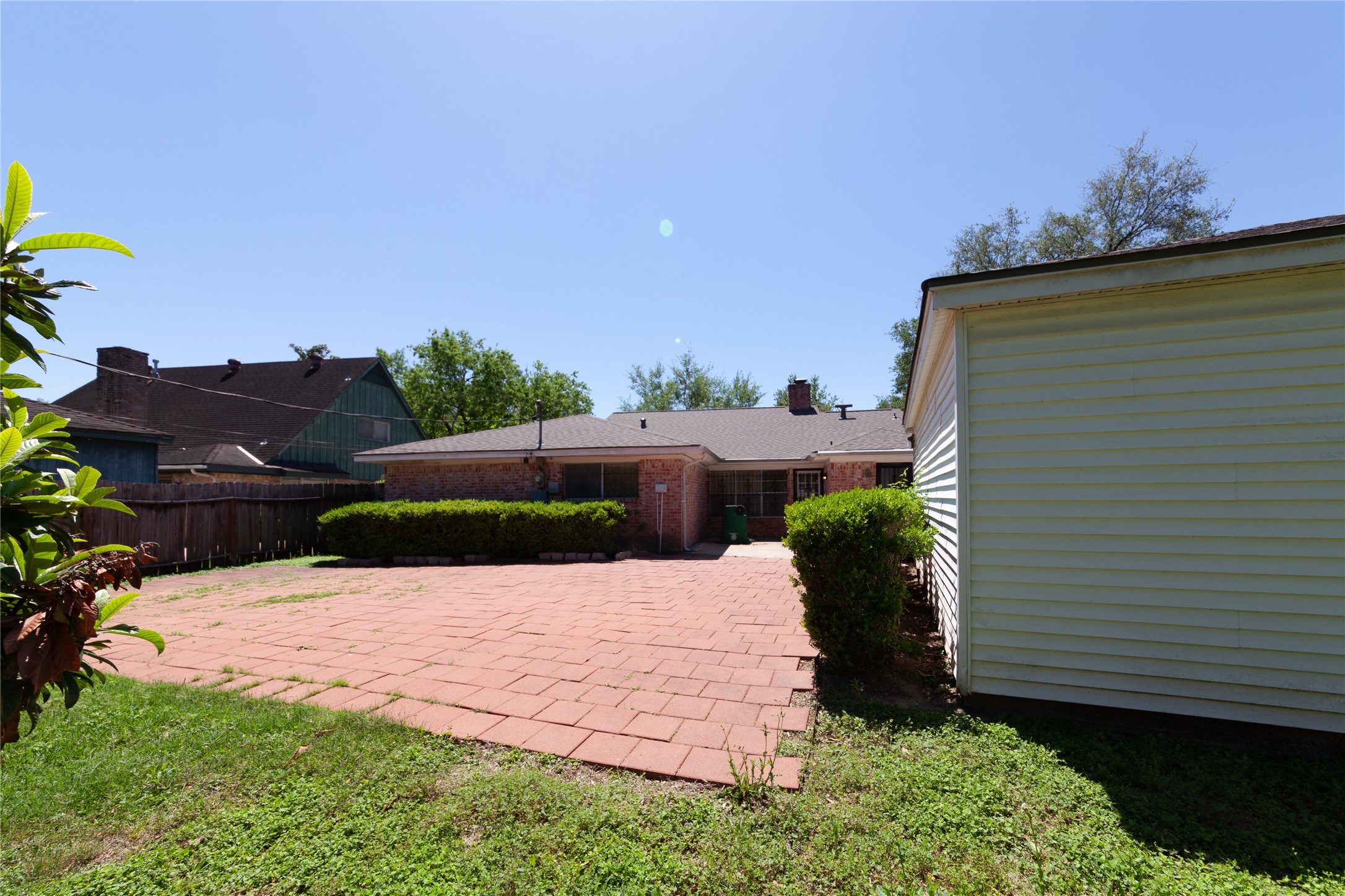 8826 Roos Road Houston, TX 77036 - Photo 42 of 42 Spacious backyard featuring a large brick patio, perfect for outdoor gatherings. The area is bordered by greenery, offering privacy and a pleasant view.