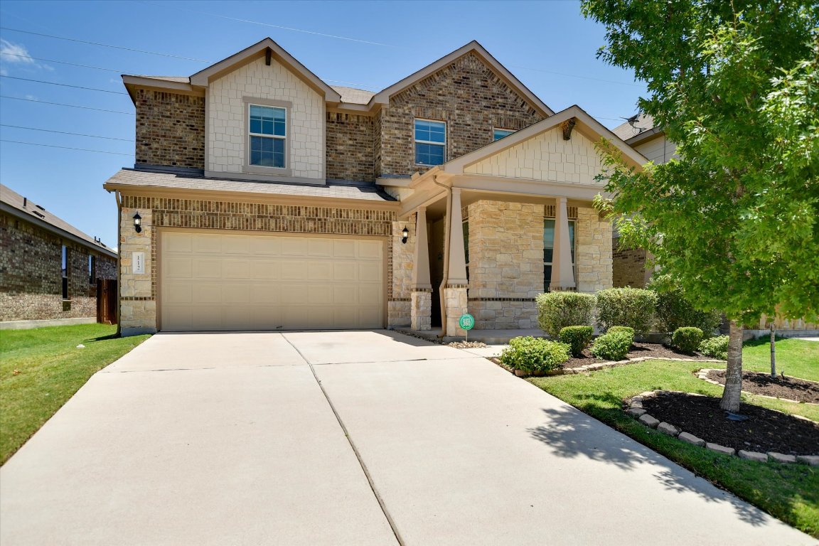 View of front facade featuring driveway, an attached garage, stone siding, covered porch, and a front yard