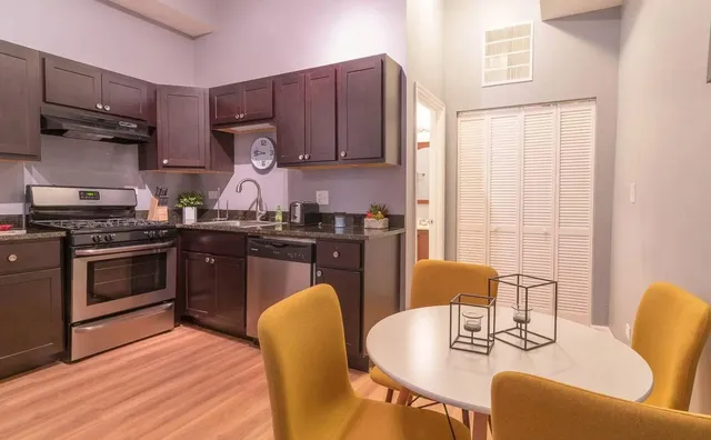 a kitchen with stainless steel appliances granite countertop a stove a sink dishwasher a dining table and chairs with wooden floor