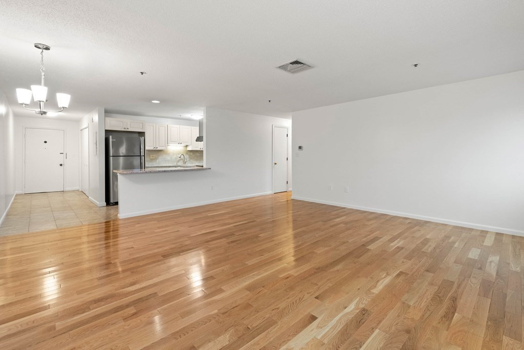 36 Dunham Road, Unit 306 Beverly, MA 01915 - Photo 9 of 26 an empty room with wooden floor and kitchen view