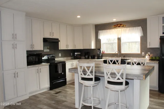 a kitchen with granite countertop a stove a sink and white cabinets