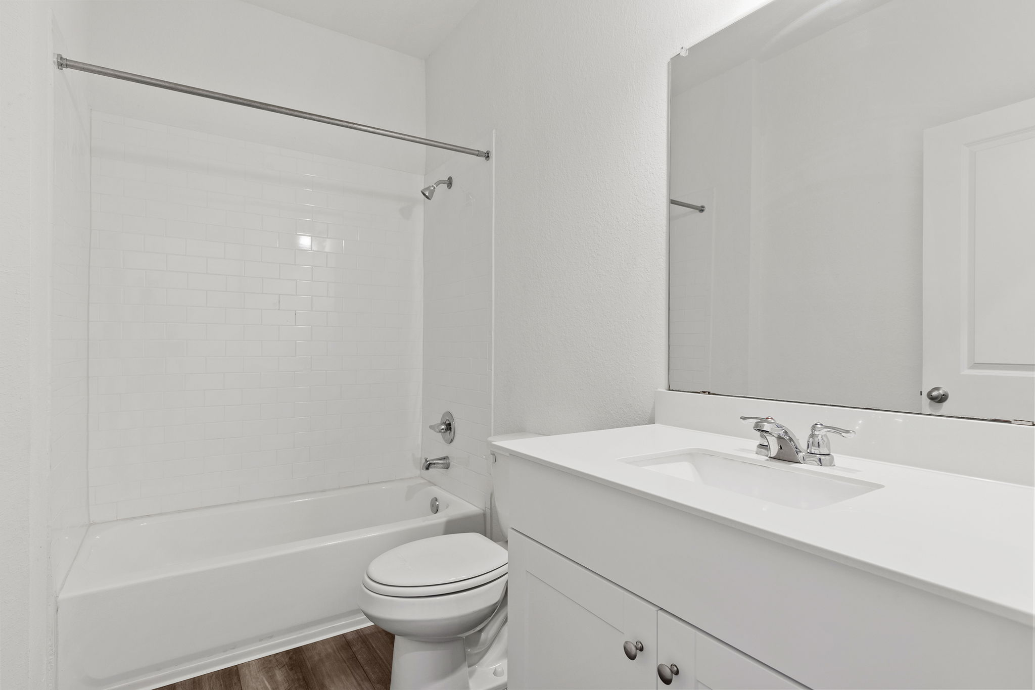 409 Line Of Fire Way Jarrell, TX 76537 - Photo 12 of 30 Contemporary bathroom featuring a white subway tile tub surround, white vanity with integrated sink, chrome fixtures, wood-finish flooring, and neutral wall paint.