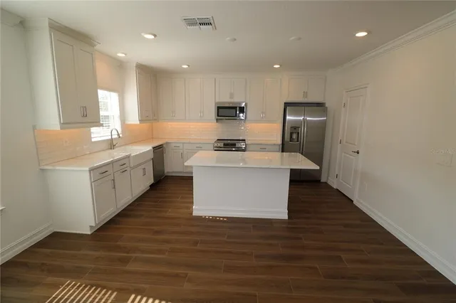a kitchen with stainless steel appliances a white refrigerator a stove a sink and white cabinets with wooden floor