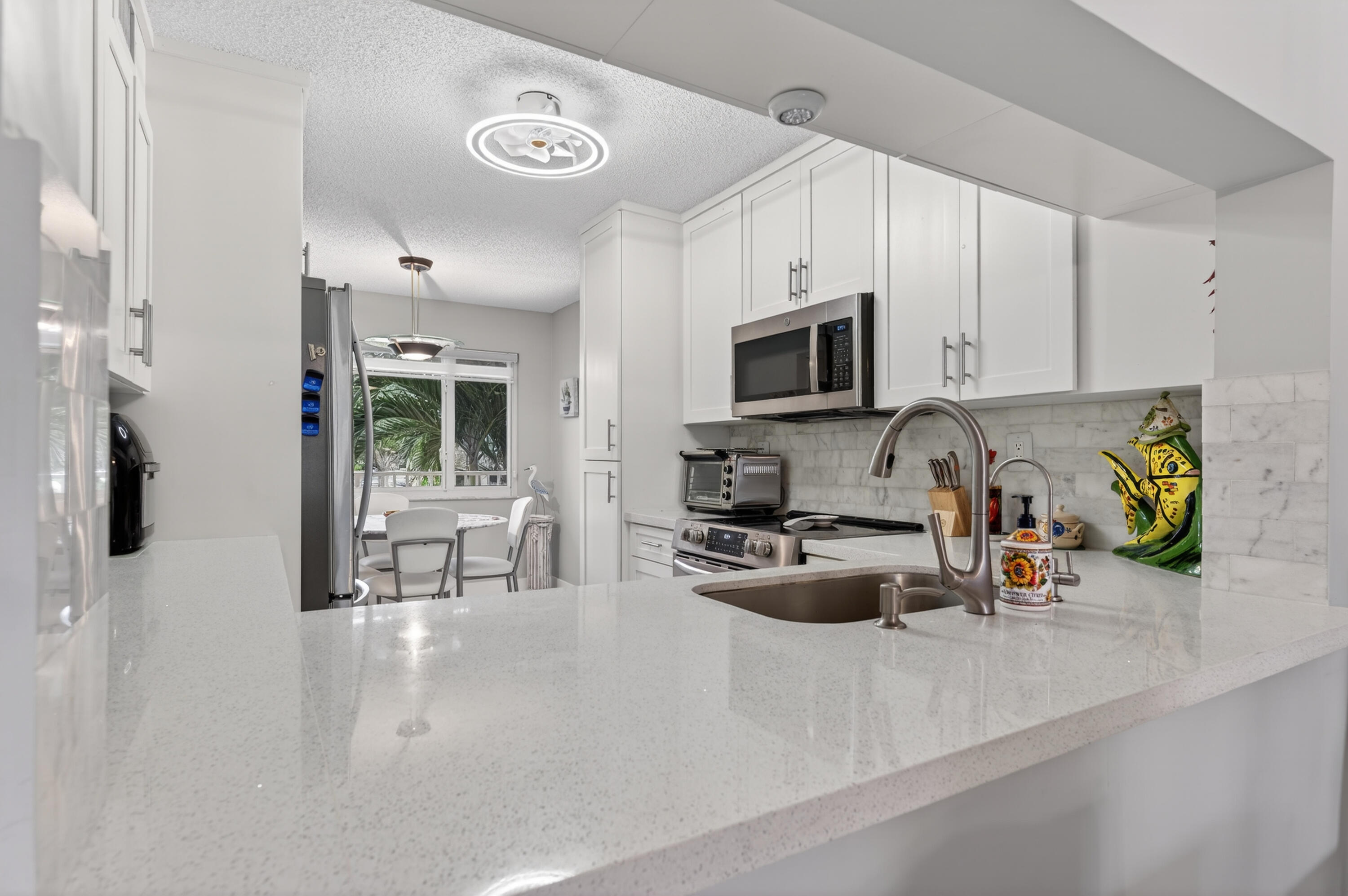 7142 South Devon Drive, Unit 210 Tamarac, FL 33321 - Photo 5 of 36 a kitchen with stainless steel appliances a stove a sink a microwave a refrigerator a dining table and chairs with white cabinets