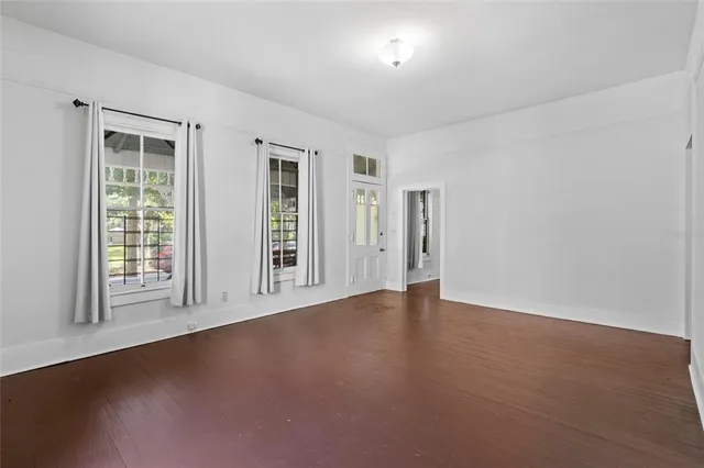 an empty room with wooden floor chandelier fan and windows