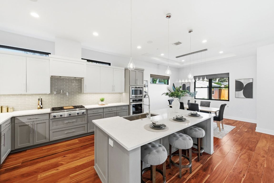 3102 Hunt Trail Austin, TX 78757 - Photo 10 of 38 Kitchen featuring gray cabinetry, decorative light fixtures, a breakfast bar area, dark wood-style flooring, and decorative backsplash