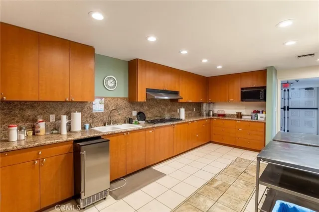 a kitchen with stainless steel appliances granite countertop a sink a stove top oven a chimney and cabinets