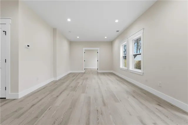 a view of empty room with wooden floor and kitchen