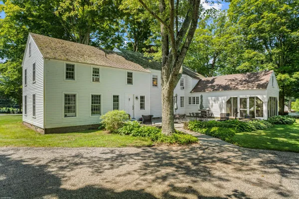 a view of a white house next to a yard with plants and large trees