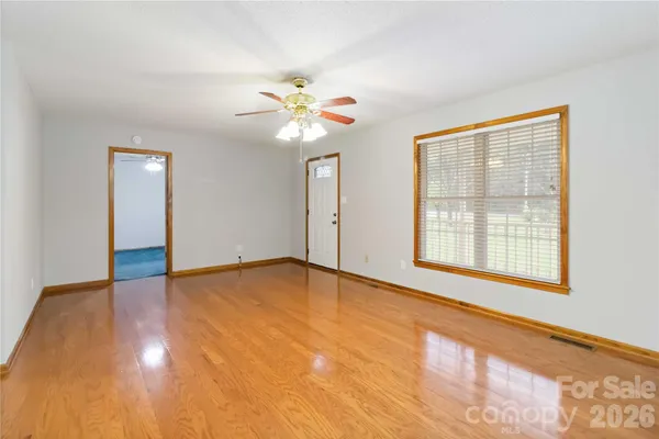 a view of an empty room with chandelier fan and wooden floor