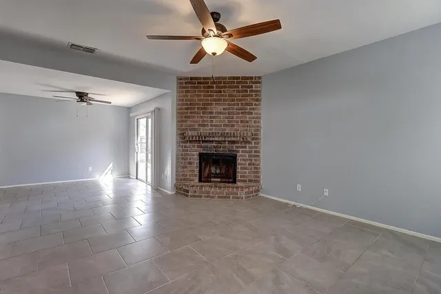 a view of an empty room with a fireplace and a ceiling fan