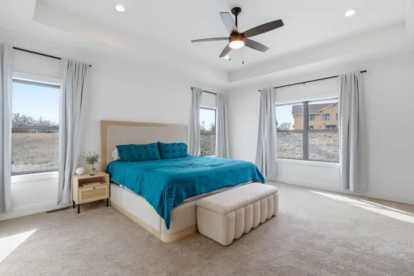 a spacious bedroom with a bed painting on wall and windows