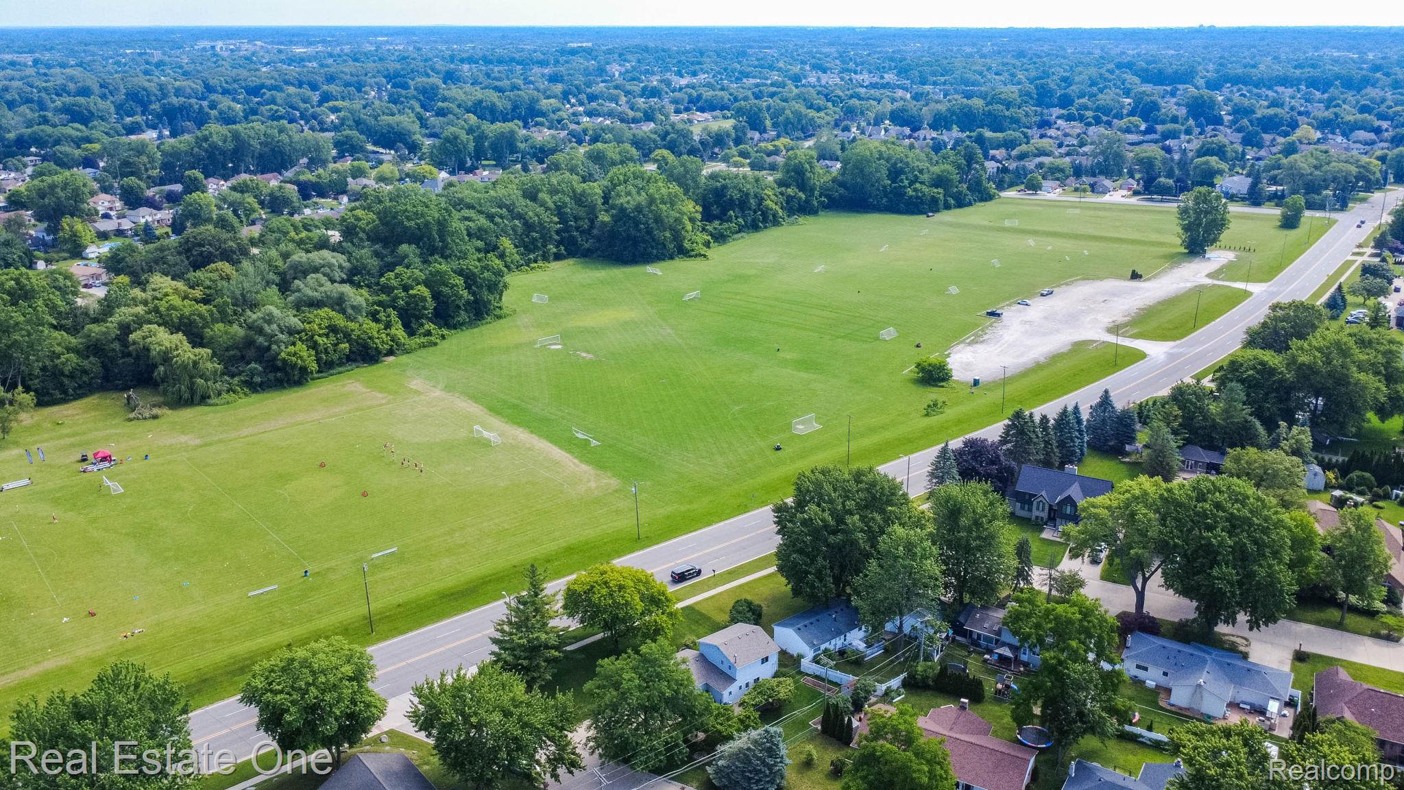 13912 Clinton River Road Sterling Heights, MI 48313 - Photo 42 of 43 Expansive green space featuring multiple marked fields, a gravel parking area, and mature perimeter trees