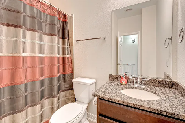 a bathroom with a granite countertop sink toilet a mirror and shower curtain