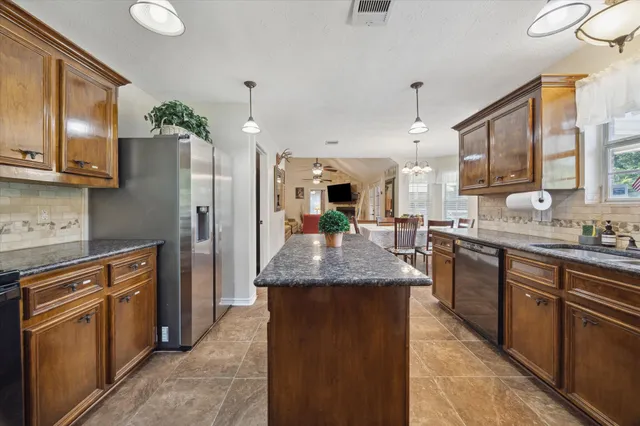 a kitchen with stainless steel appliances granite countertop a refrigerator a sink dishwasher a oven and a dining table with wooden floor