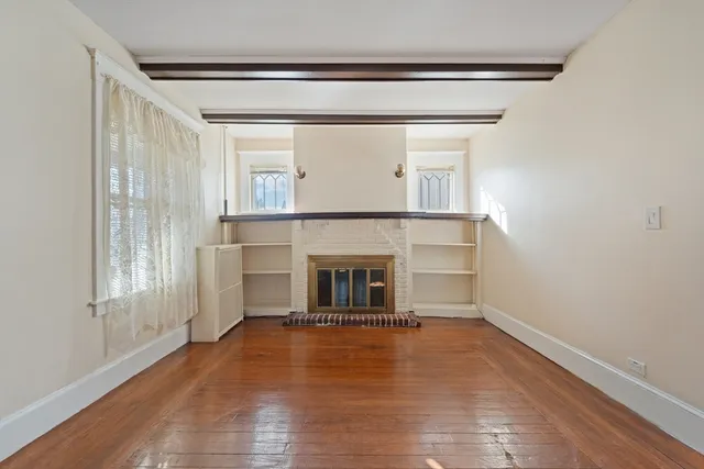 an empty room with wooden floor fireplace and windows