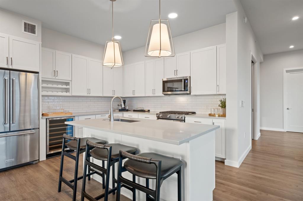 3111 Sunset Boulevard, Unit 915 Flower Mound, TX 75022 - Photo 6 of 39 a kitchen with stainless steel appliances a stove a sink island and a refrigerator with wooden floor