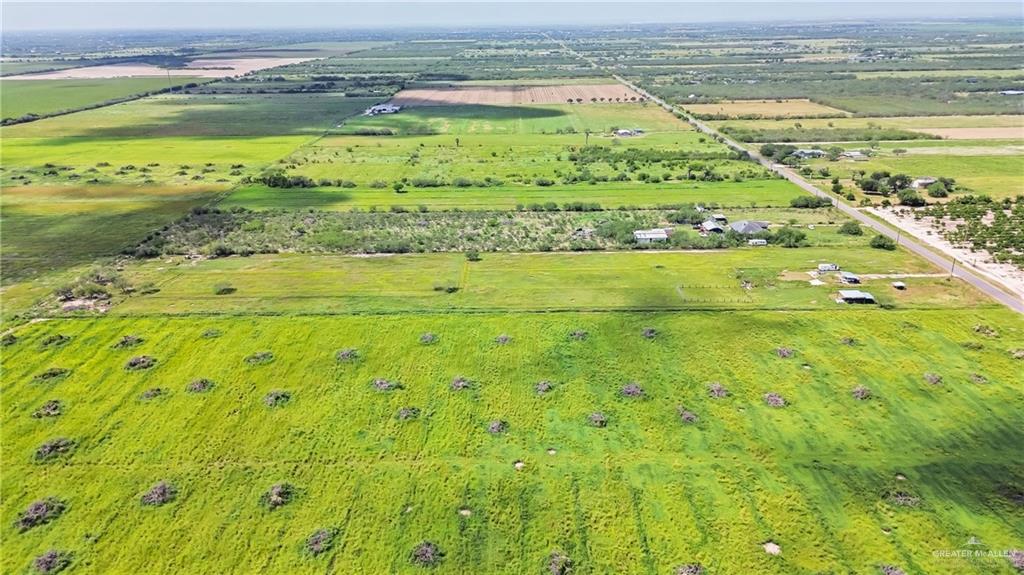 27870 North Western Road Mission, TX 78574 - Photo 7 of 8 Expansive agricultural land featuring a verdant field, scattered natural vegetation, a paved road, and distant structures