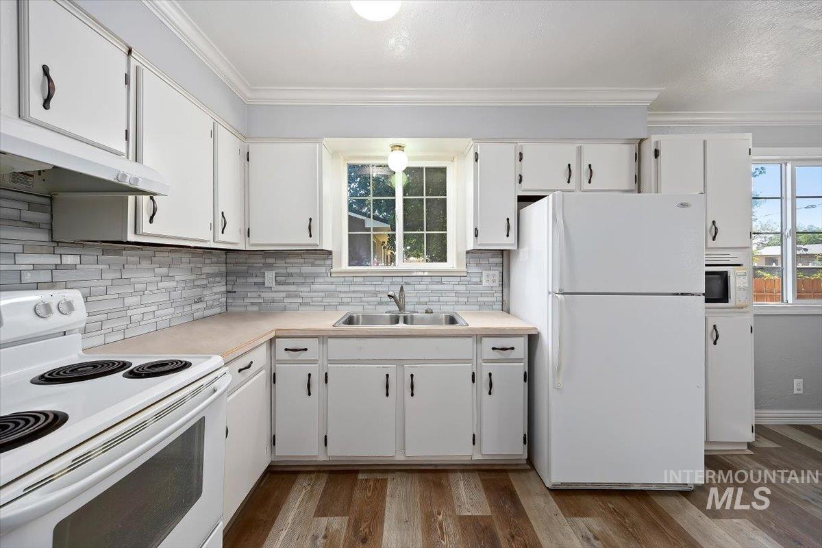 1940 Q Street Heyburn, ID 83336 - Photo 15 of 30 Kitchen featuring wood-finish flooring, white cabinetry with dark hardware, light-toned countertops, and a subway tile backsplash
