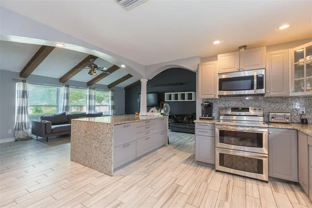 a living room with stainless steel appliances furniture wooden floor and a kitchen view