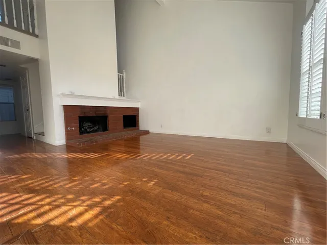 an empty room with wooden floor fireplace and windows