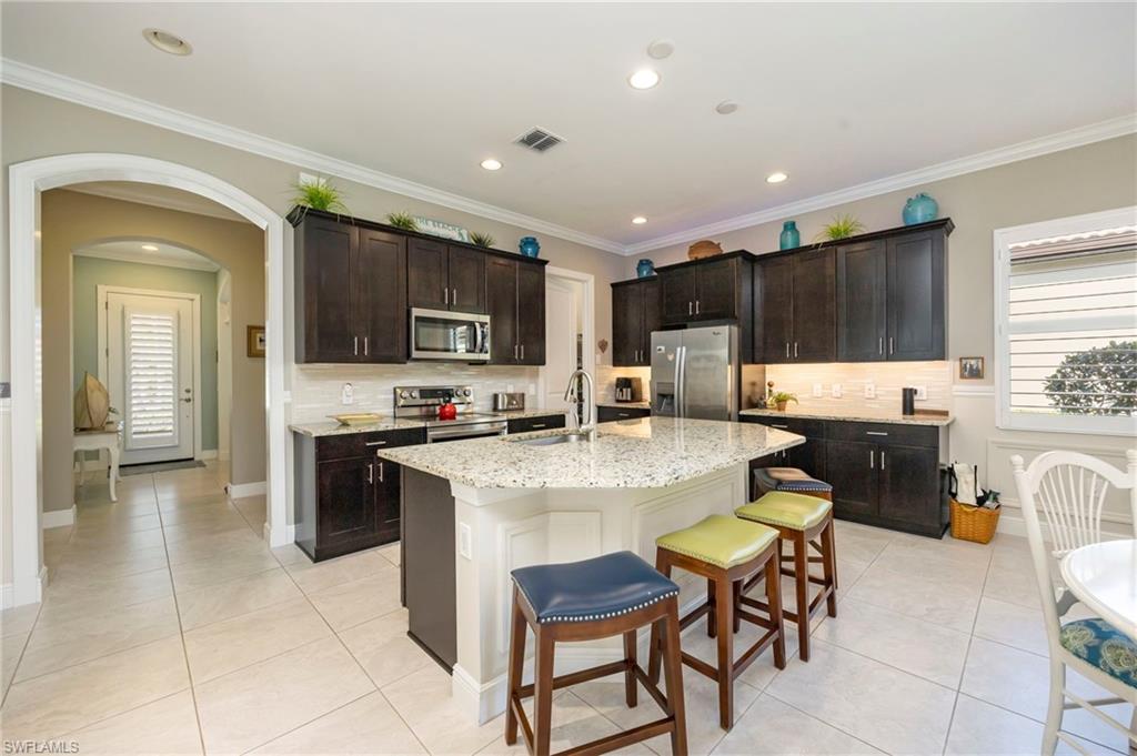 1287 Manado Drive Naples, FL 34113 - Photo 7 of 32 a kitchen with kitchen island granite countertop a stove a sink a microwave a dining table and chairs