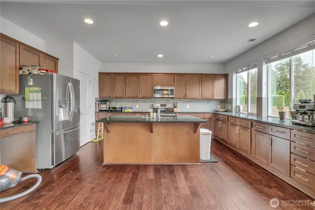 a kitchen with stainless steel appliances granite countertop a refrigerator a sink dishwasher a stove and white countertops with wooden floor