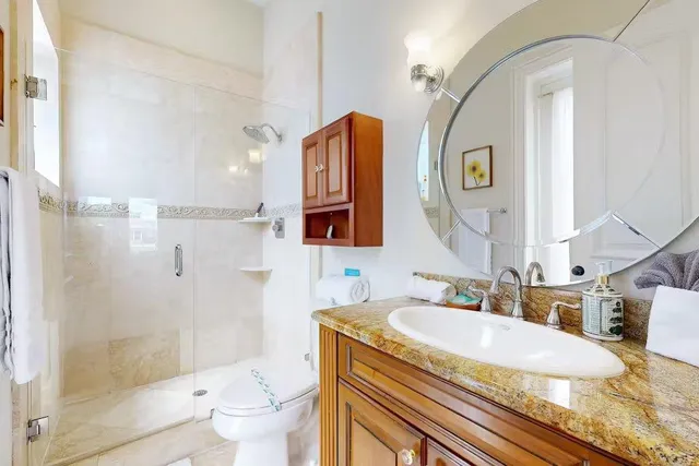 a bathroom with a granite countertop sink a mirror a toilet and shower