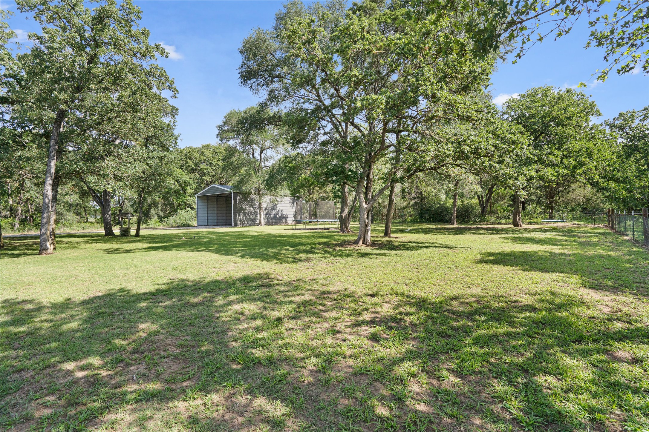 136 Fawn Hollow Elgin, TX 78621 - Photo 36 of 40 Expansive outdoor space featuring a metal shed structure, mature trees, and a perimeter fence