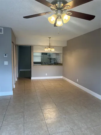 a view of an empty room and chandelier fan and kitchen view