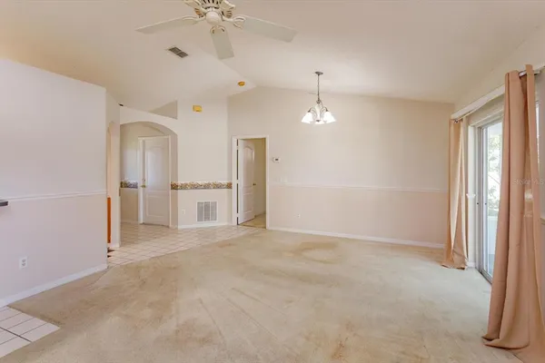 an empty room with chandelier fan and windows