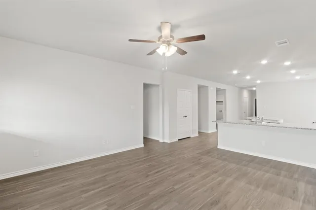 a view of an empty room with wooden floor and a ceiling fan