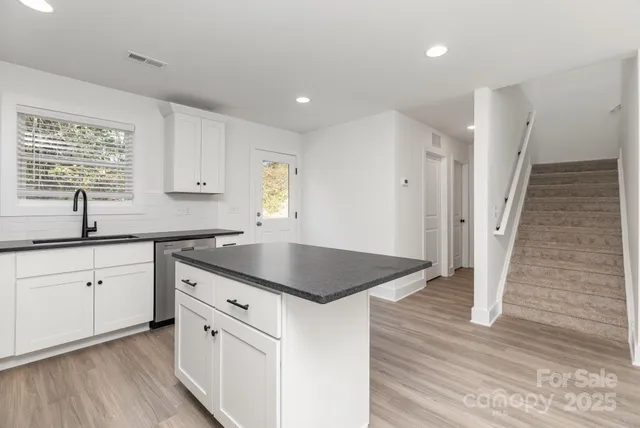 a kitchen with white cabinets a sink dishwasher and a stove with wooden floor