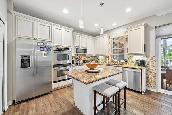 a kitchen with granite countertop kitchen island stainless steel appliances a table chairs sink and wooden floor