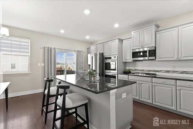 a kitchen with stainless steel appliances granite countertop a stove top oven a sink a refrigerator with grey cabinets and wooden floor