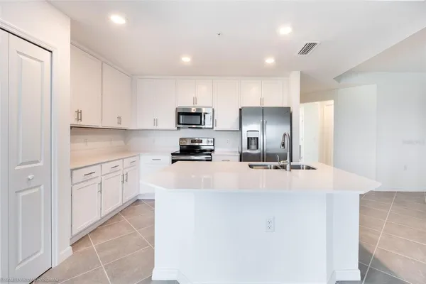 a large kitchen with kitchen island a sink a stove a refrigerator and white cabinets