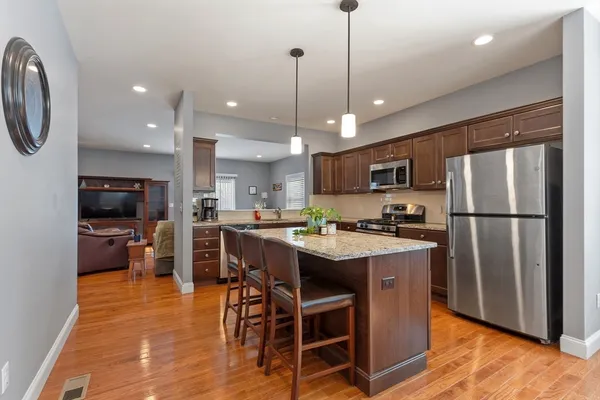 a kitchen with stainless steel appliances granite countertop a refrigerator a stove top oven a sink dishwasher a dining table and chairs with wooden floor