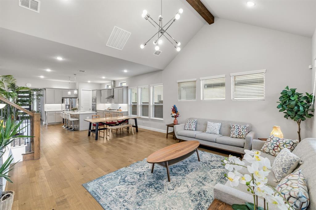 7852 Buffaloberry Road Frisco, TX 75035 - Photo 14 of 36 Spacious open-concept living area featuring high vaulted ceilings with a visible wood beam, wood-finish flooring, and multiple windows