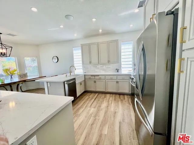 a kitchen with stainless steel appliances granite countertop a refrigerator a stove a sink a dining table and chairs with wooden floor